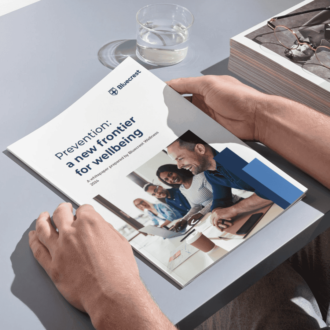 Someone holding a book, the cover says "Prevention: a new frontier for wellbeing" and is a paper by Bluecrest Wellness.