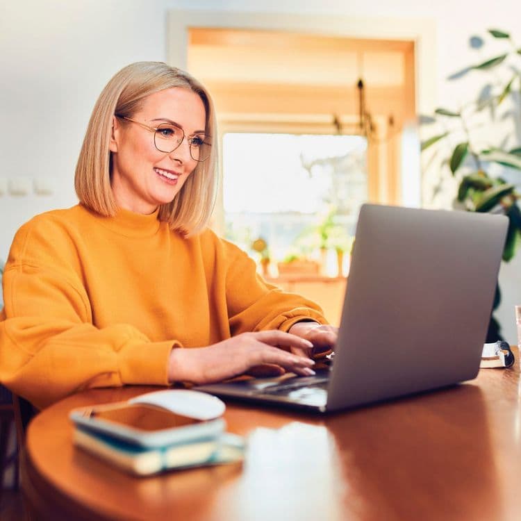 A woman in an orange jersey typing on a laptop.