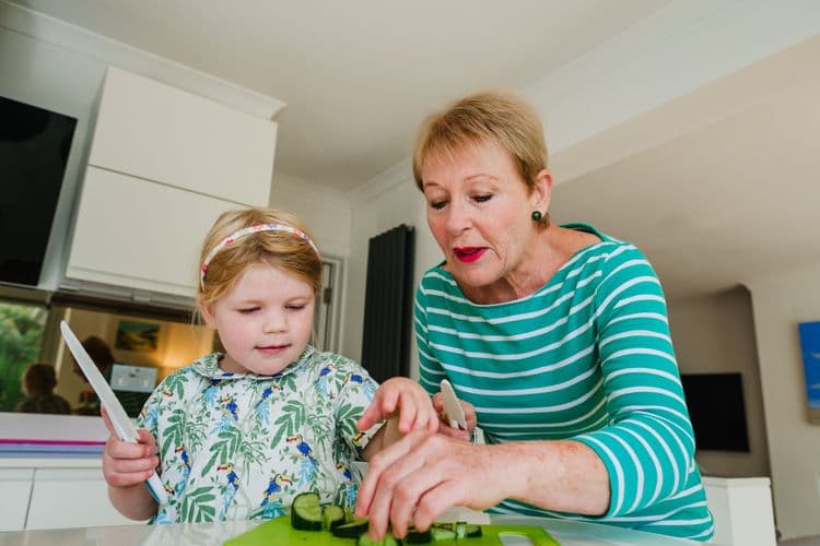 Grandma helping her granddaughter cut cucumbers.