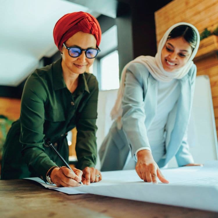 Two women wearing headscarves working on a blueprint together.
