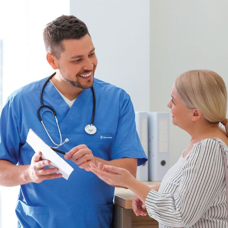 Doctor in blue scrubs showing a patient something on a piece of paper.