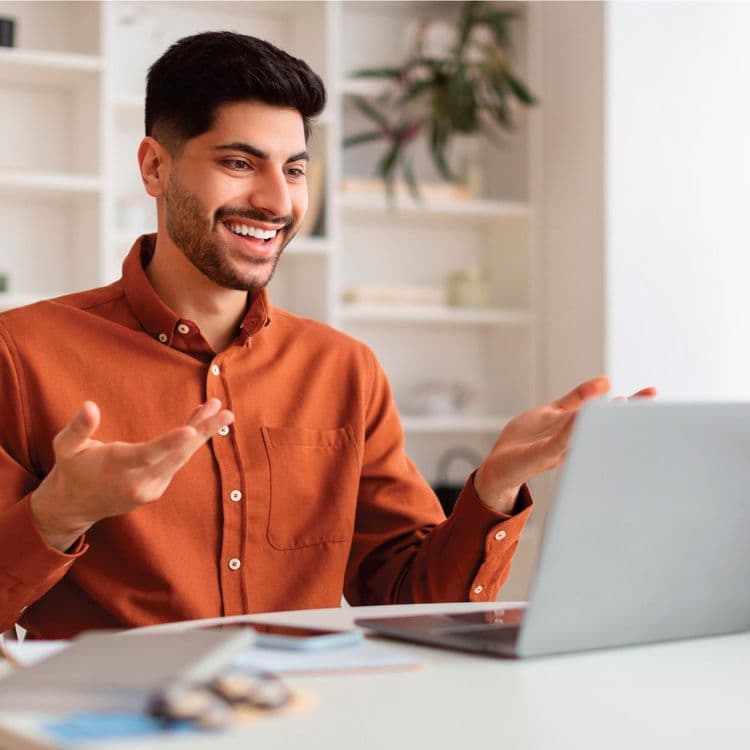 Man in an orange button-up shirt in a virtual meeting on his laptop.